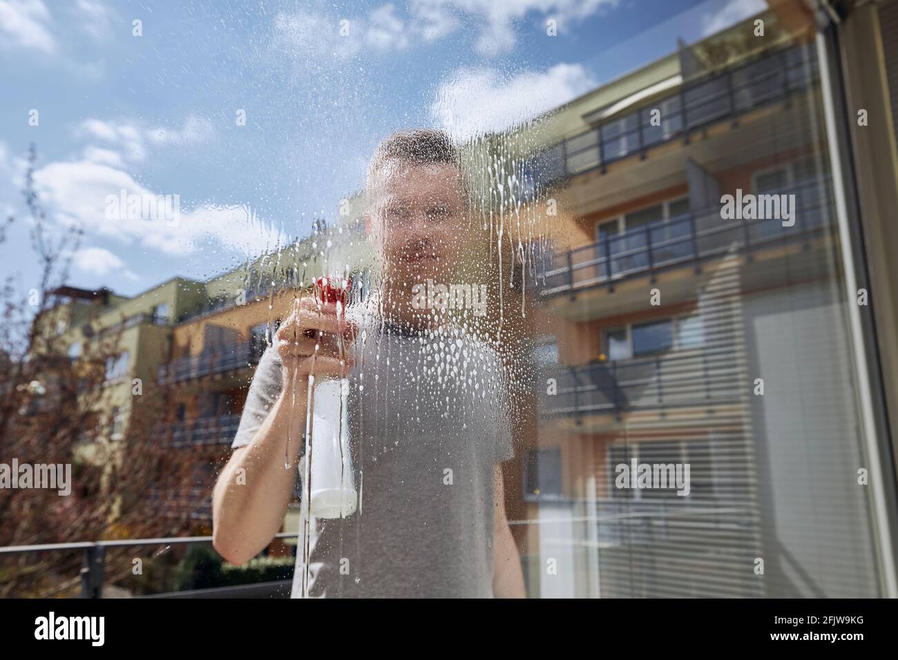 Mann putzt Fenster mit Reinigungsspray zu Hause. Themen Hausarbeit und Housekeeping. Stockfoto