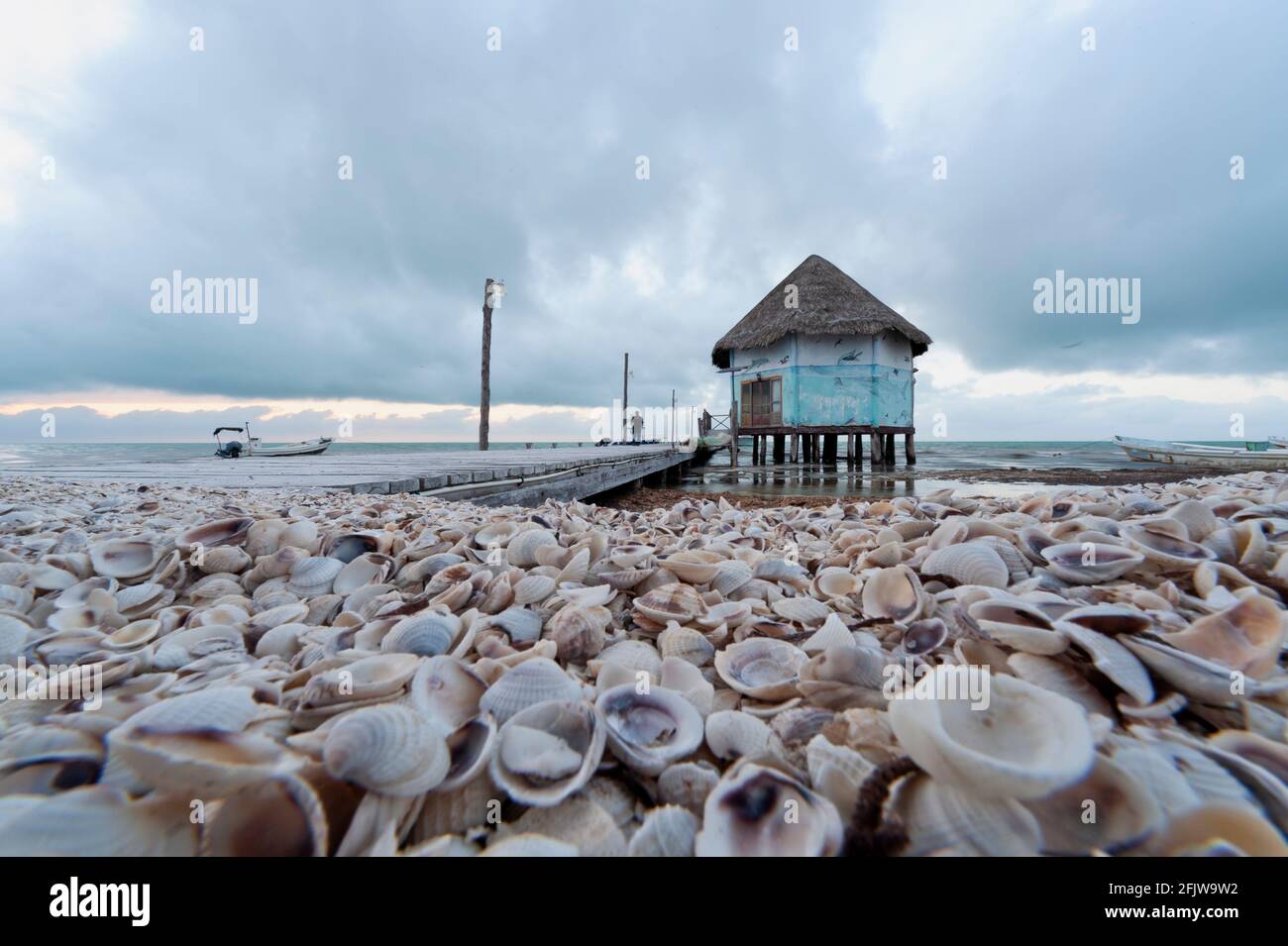 Nahaufnahme eines Muschelstrandes auf Holbox Island in Mexiko, mit dem alten hölzernen Pier an der Karibik. Im Hintergrund der dramatische Wolkenhimmel. Stockfoto