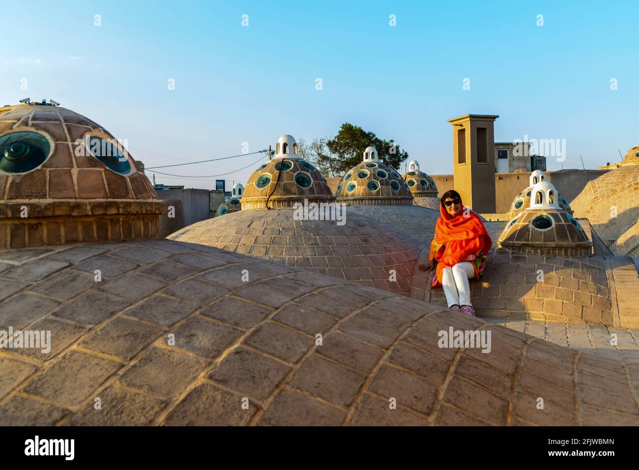 Lady mit orangefarbenem Schal sitzt auf dem Dach mit mehreren Kuppeln des Sultan Amir Ahmad (oder Qasemi) Badehaus. Kashan, Iran. Stockfoto