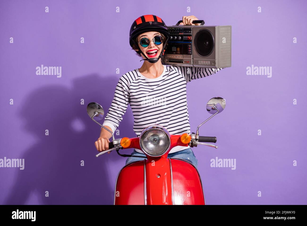 Portrait Foto von lachenden Mädchen in Helm Motorrad lächelnd halten boombox isoliert auf hellviolettem Hintergrund Stockfoto