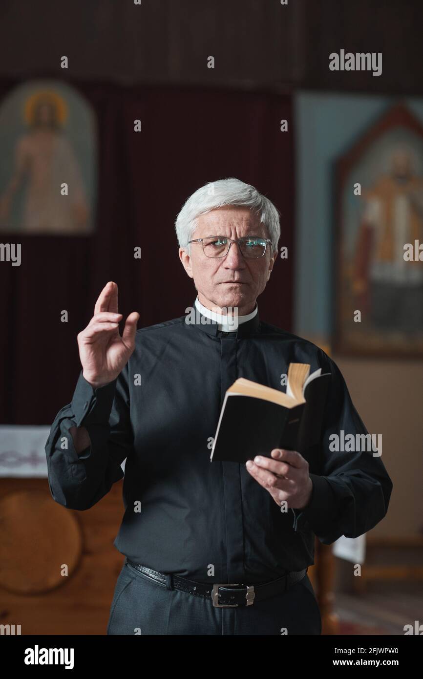 Porträt eines älteren Priesters, der während einer Messe die Bibel liest In der Kirche Stockfoto