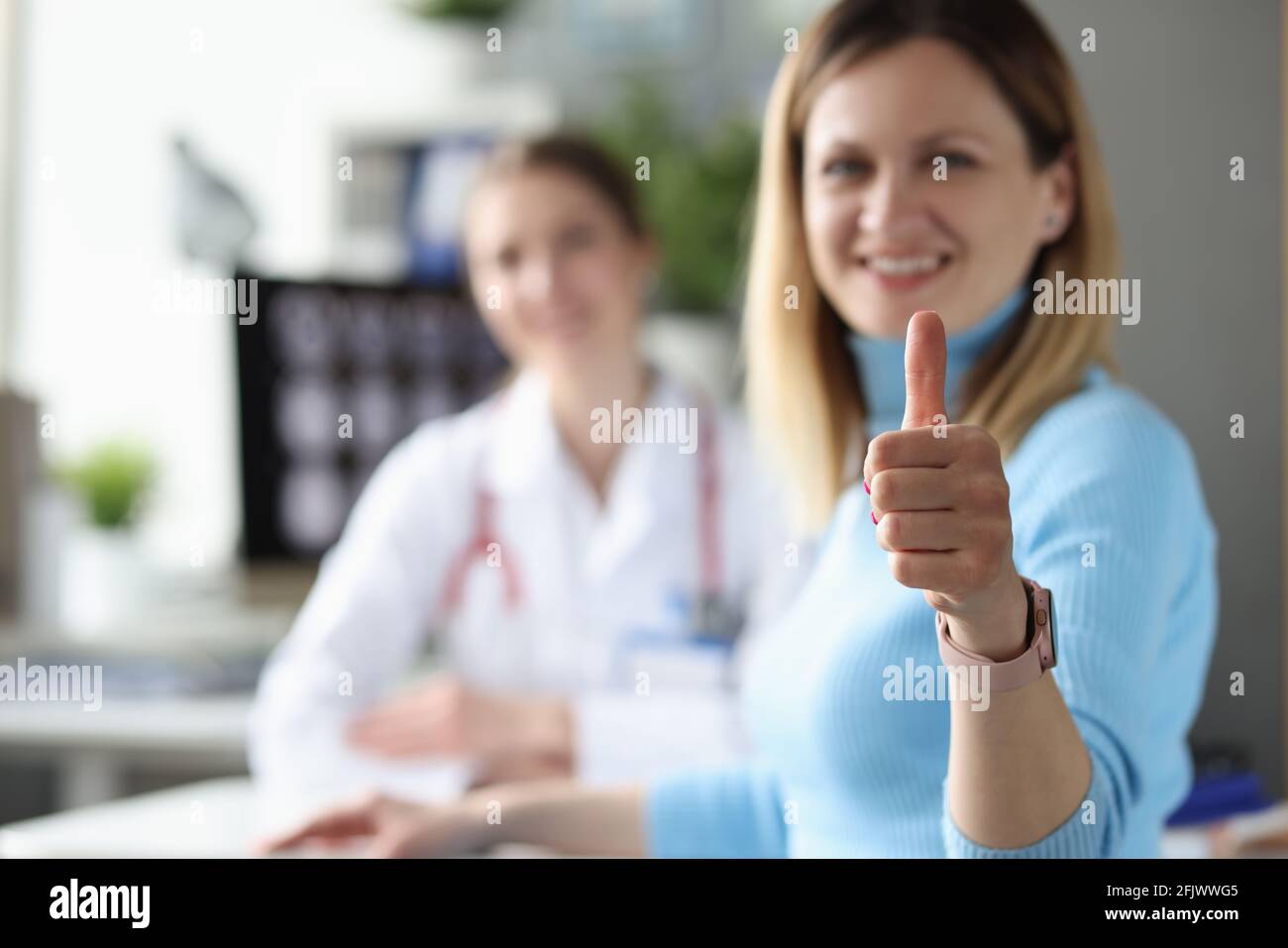 Eine Patientin zeigt beim Arzttermin eine Geste mit dem Daumen nach oben Stockfoto