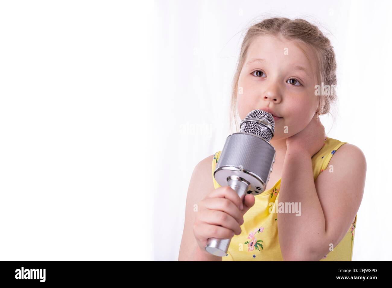 Ein blondes kleines Mädchen singt in ihren Händen ein Lied in ein Mikrofon.  Ein schönes Kind zeigt seine aufrichtigen Gefühle von Glück und positiv.  Geflochtene Haare Stockfotografie - Alamy