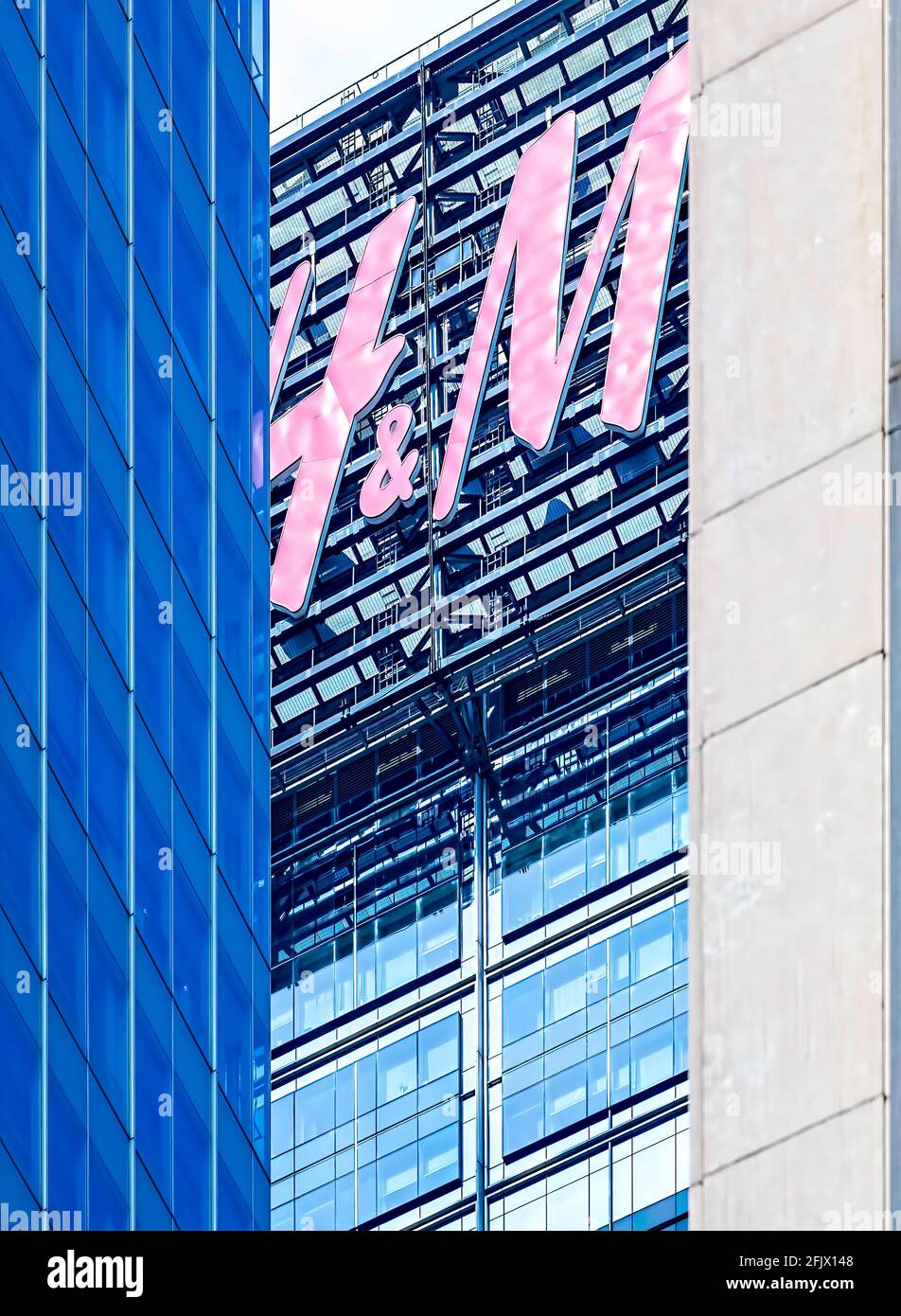 Das rote „H&M“-Schild auf der 151 West 42nd Street schaut zwischen gegenüberliegenden Gittern aus blauem Glas und weißem Beton der Times Square-Wolkenkratzer hervor. Stockfoto