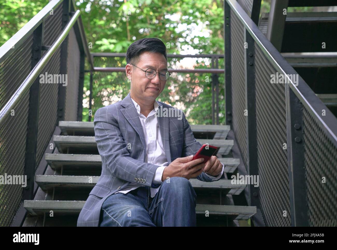 Geschäftsmann sitzt auf der Treppe und surft in seinem Telefon. Urban mit grünem Hintergrund. Stockfoto