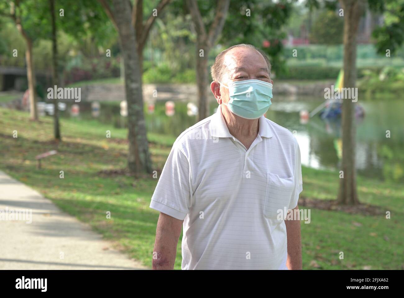 Älterer asiatischer Mann mit Gesichtsmaske, der morgens im Park spazieren ging. Stockfoto