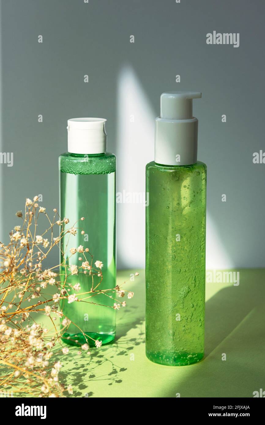 Grüne Kosmetikflaschen mit Gesichtswaschgel und Tonic auf grünem Tisch. Trockene Gypsophila Blumen Dekoration. Natürliche Bio-Kosmetik-Konzept Stockfoto