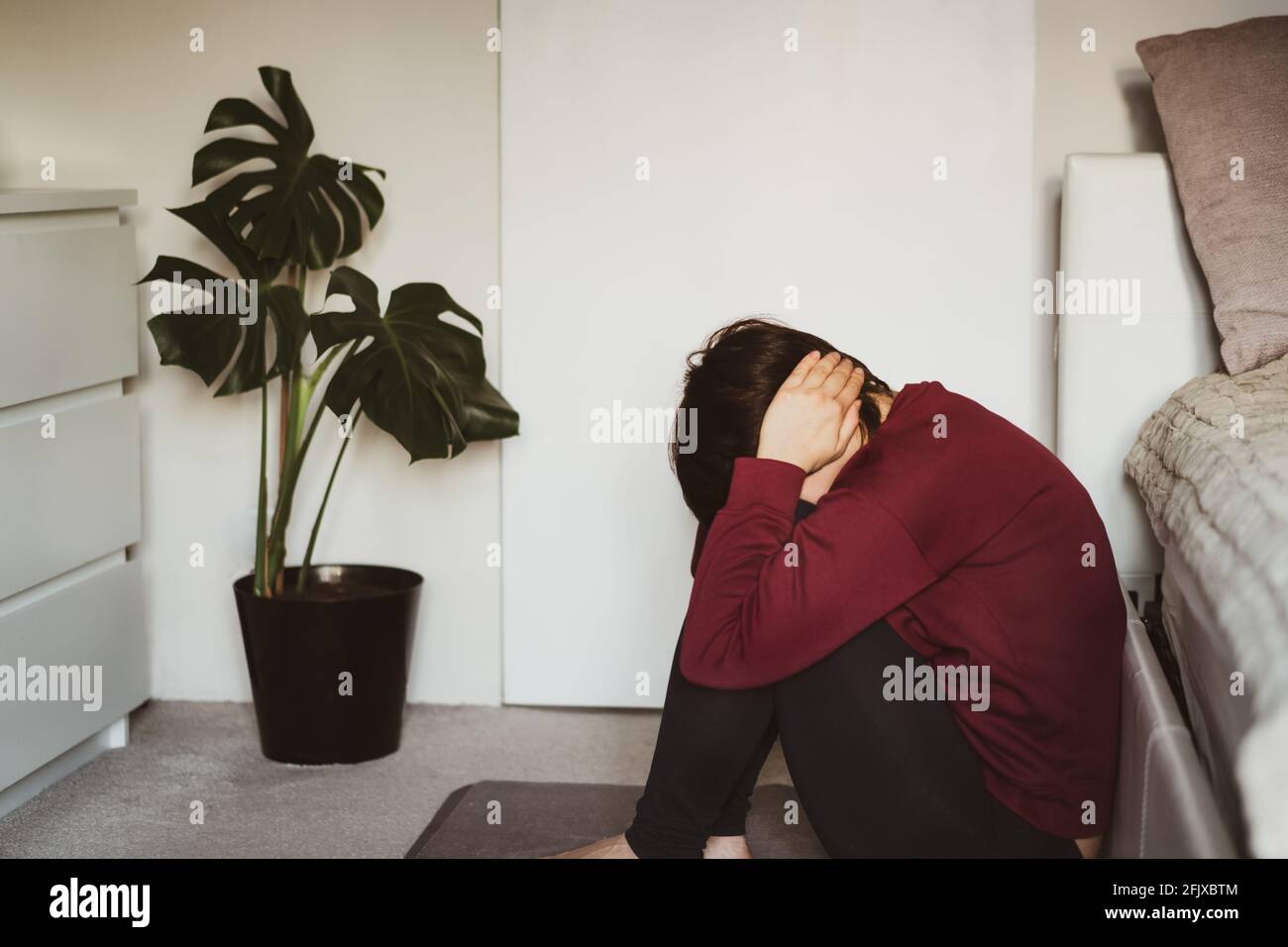 Depressive und traurige Frau, die ihren Kopf mit Händen bedeckte und im Schlafzimmer auf dem Boden saß. Beunruhigt durch häusliche Gewalt, unwillige Schwangerschaft Stockfoto