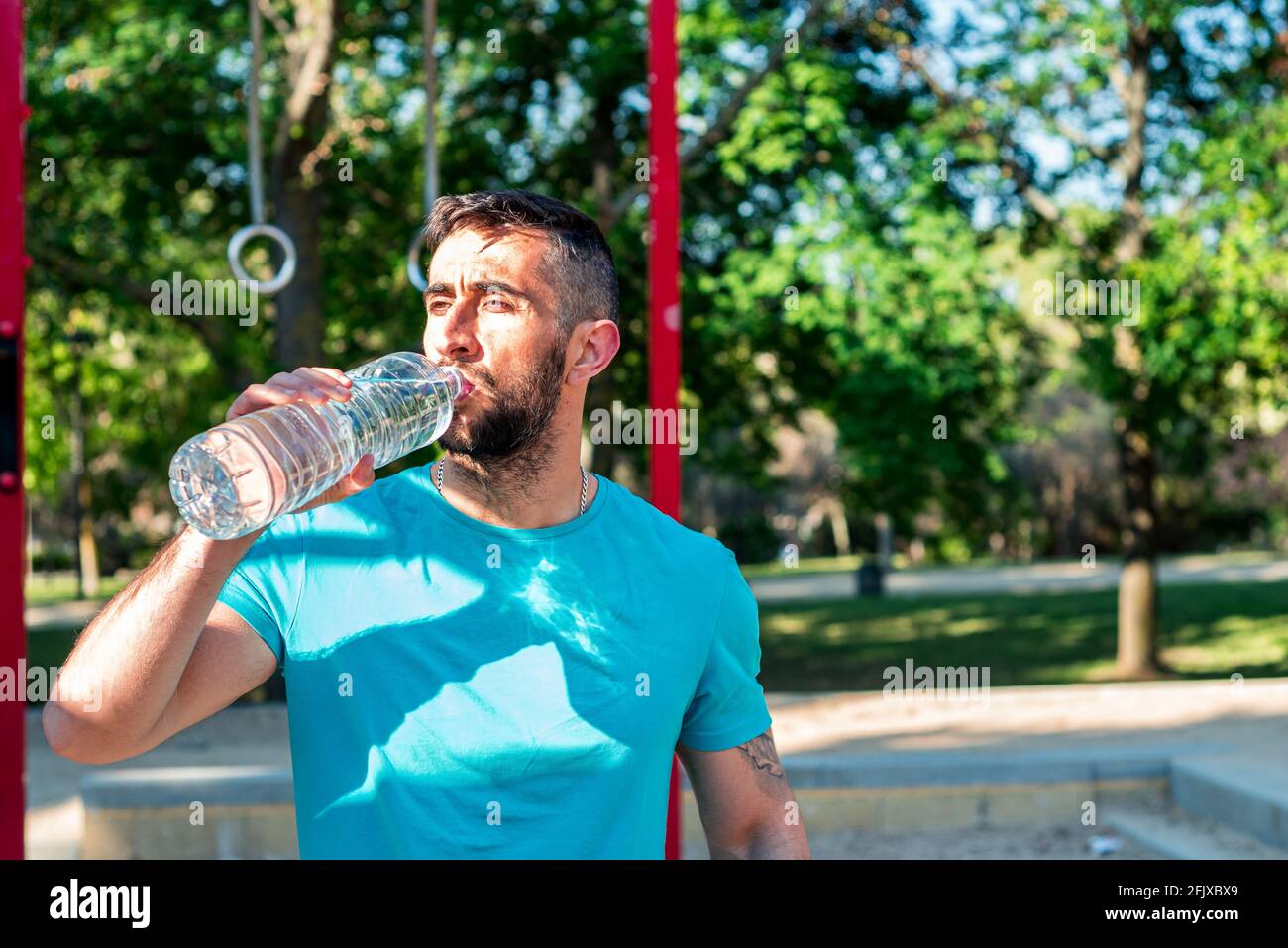 Bärtiger Brunette Mann, der nach dem Training in einem Park Wasser trinkt. Fitnesskonzept im Freien. Stockfoto