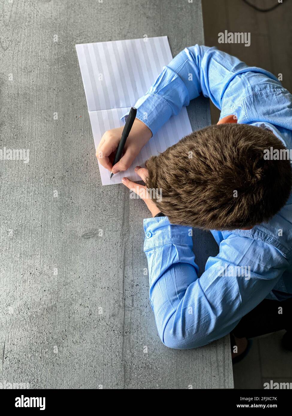 Junge in einem blauen Hemd schreibt in einem Notizbuch, freier Platz Stockfoto