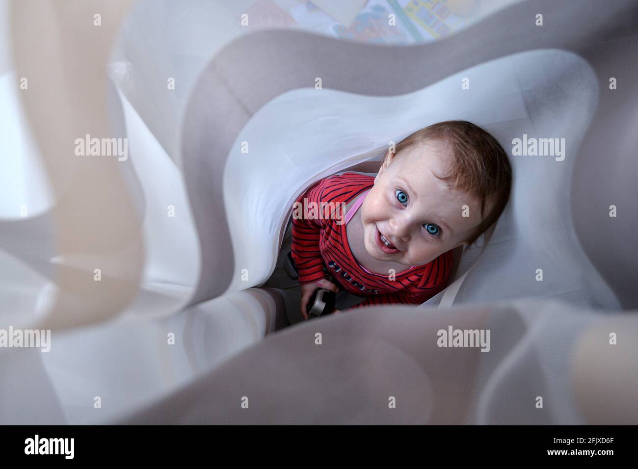 Lächelndes kleines Mädchen, das sich in Vorhängen versteckt Stockfoto