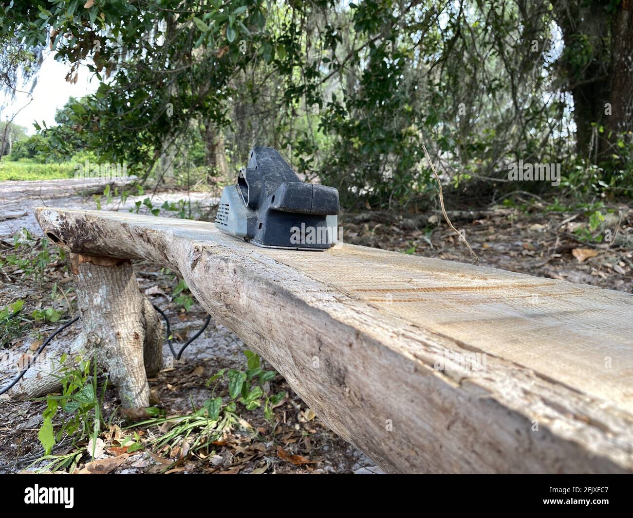 Schleifmaschine zum Abschleifen einer handgefertigten Holzbank für einen Outdoor-Park. Industriearbeit. Stockfoto