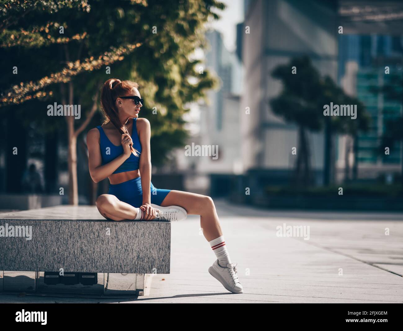Sportliche Läuferin sitzt nach dem Workout auf der Straße Steinbank. Athletic Mädchen in Sportswear tun Sport-Übungen Stockfoto