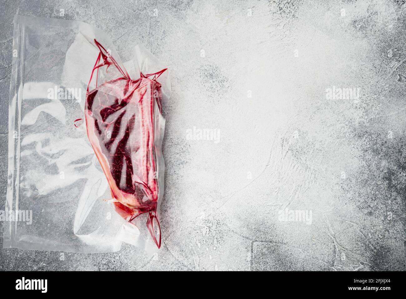 Frisches, marmoriertes Fleisch, schwarzes angus-Steak in Vakuum-Plastiktüte für Sous-Vide-Set, auf grauem Steinhintergrund, Draufsicht flach liegend, mit Platz für Text Stockfoto