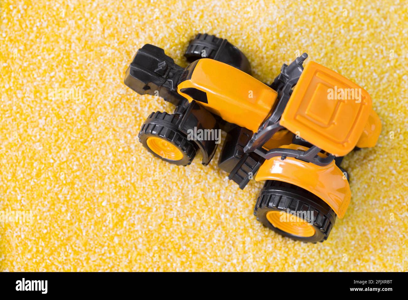 Gelber Mini-Traktor fährt auf Polenta, gelbes Maismehl, Grießkörner, Konzeptfoto Stockfoto