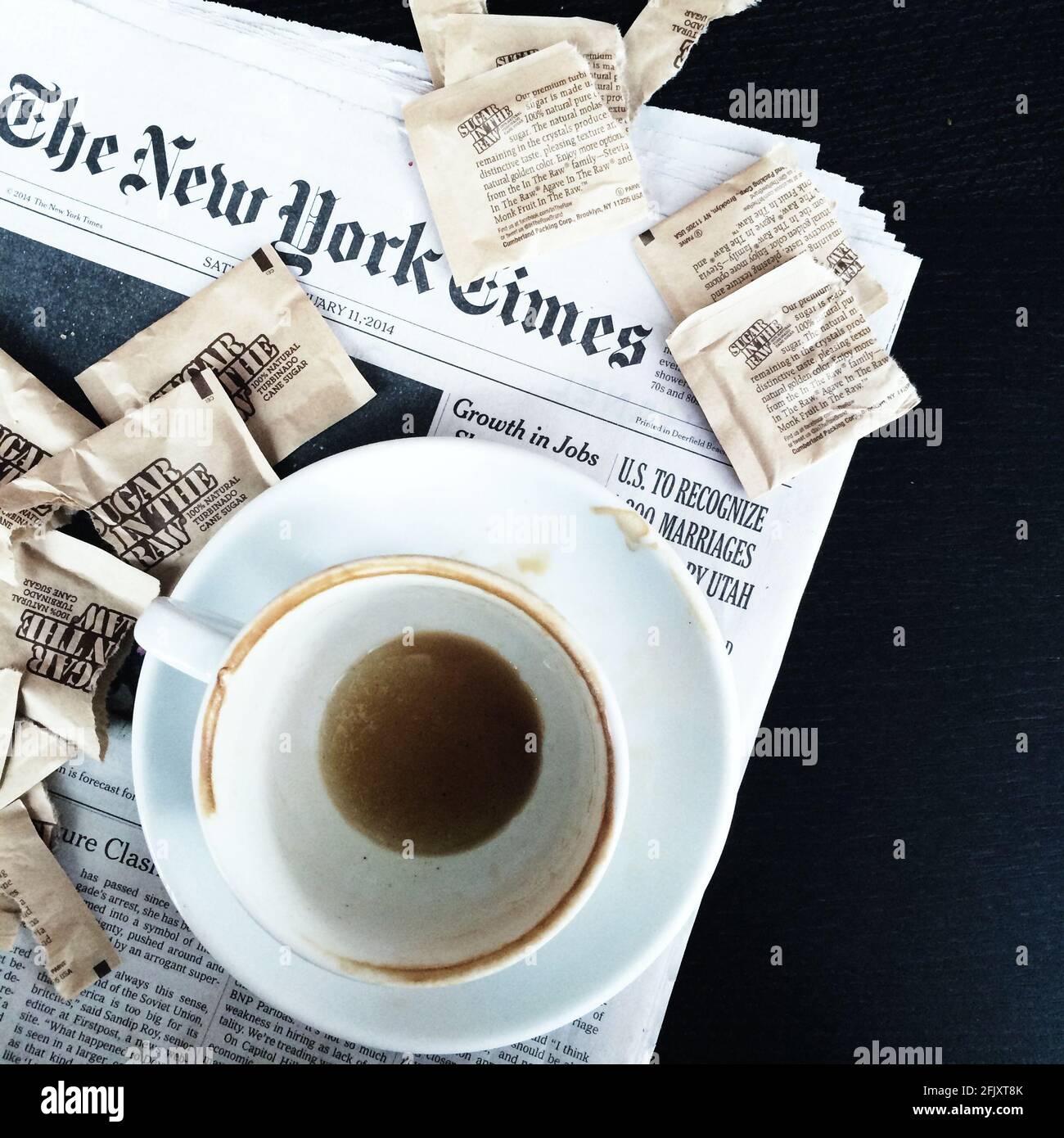 Eine schmutzige Tasse Kaffee, leer mit Kaffeemarken, die auf der New York Times Zeitung sitzen, und Zuckerpakete von Sugar im Rohkost umgeben sie Stockfoto