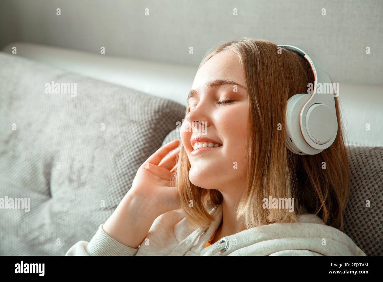 Glückliche junge Frau, die auf dem Sofa in Kopfhörern sitzt. Frau oder Teenager-Mädchen ausruhen, Glückseligkeit genießen Sie Musik auf der Couch zu Hause Innenraum des Wohnzimmers hören Stockfoto