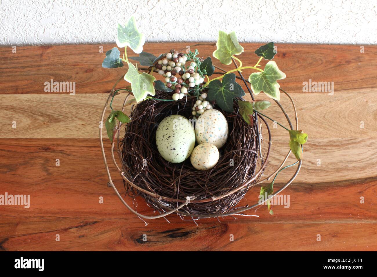 Federabbildung. 3 kleine bunte Eier in einem Kiefernnest zu Ostern, grüne Blätter und Zweige ringsum auf einem Holztisch Stockfoto