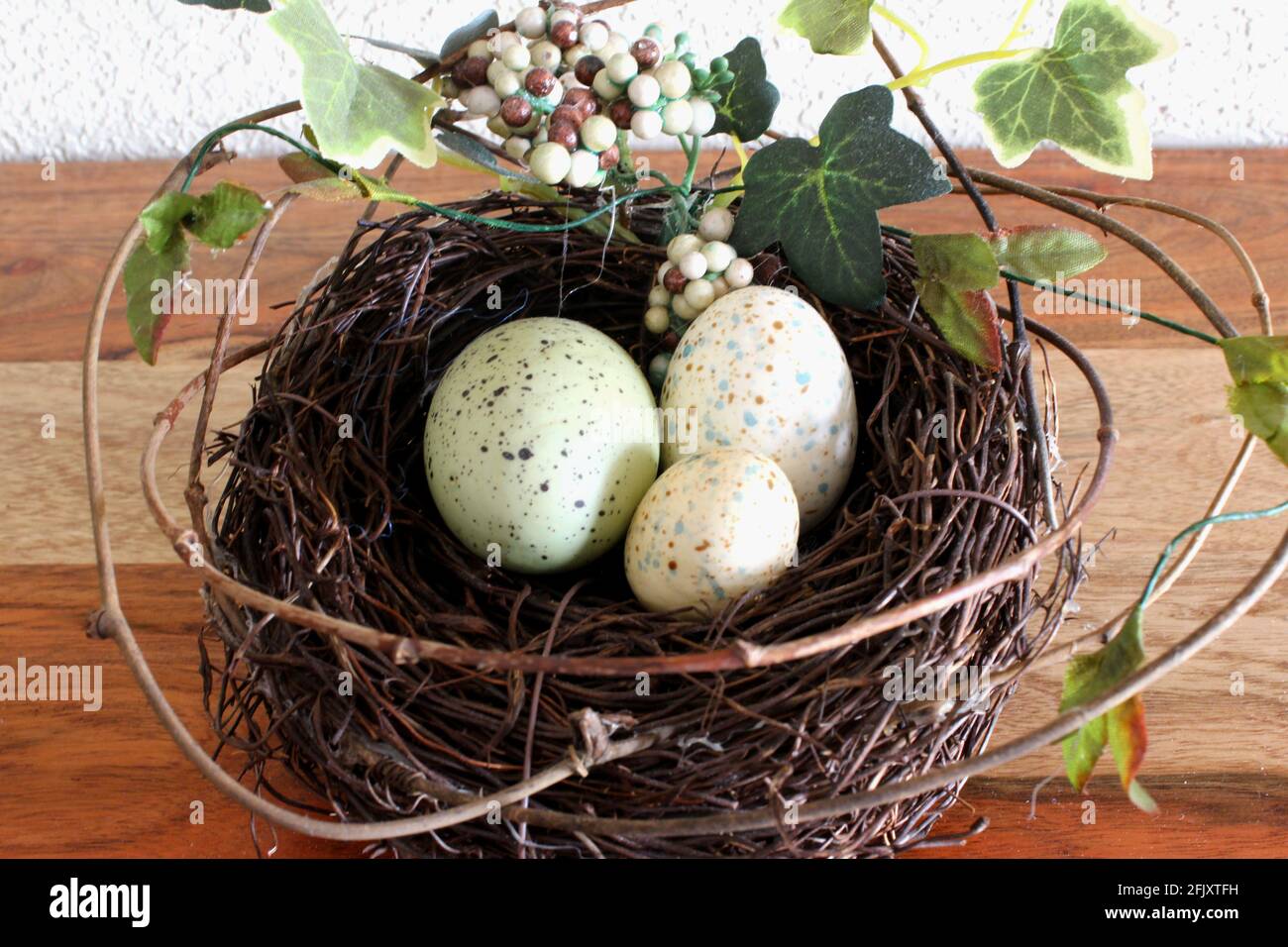 Federabbildung. 3 kleine bunte Eier in einem Kiefernnest zu Ostern, grüne Blätter und Zweige ringsum auf Holztisch, Nahaufnahme Stockfoto