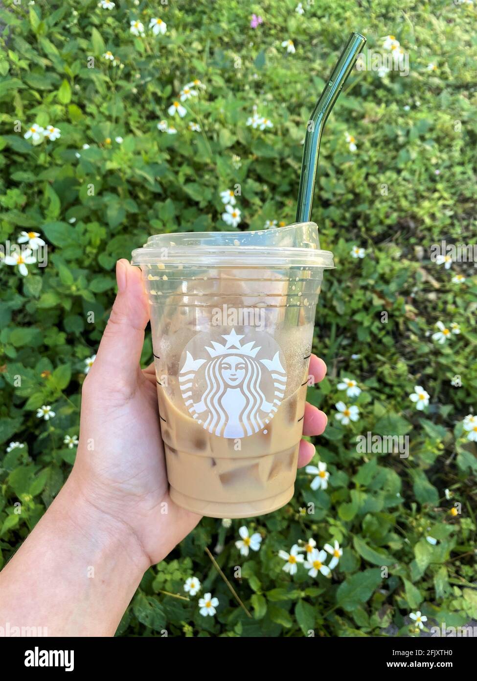 Das Halten eines Glashalms in einer Starbucks Kaffeetasse sollte die Notwendigkeit von Einweg-Plastikhalmen reduzieren, indem wiederverwendbare Strohhalme verwendet werden. Grünes Gras Hintergrund Stockfoto