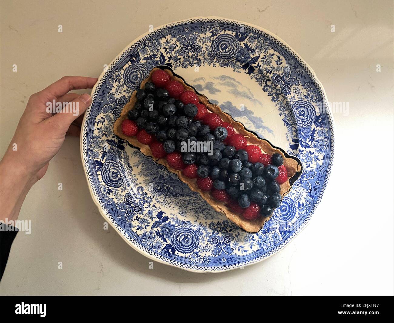 Die Hand der Frau hält eine Heidelbeer- und Himbeerherbe auf einem Dessertteller in einer Küchentheke mit einigen Schatten. Stockfoto