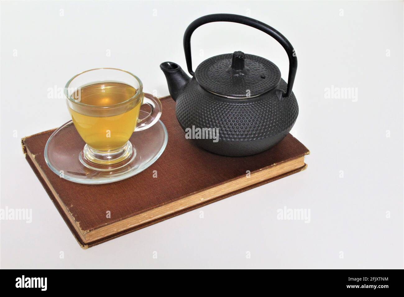 Eiserne japanische Teekannen und eine Tasse Kräutertees in einer Glas-Teetasse, serviert auf einer Untertassenplatte, die auf einem alten Jahrbuch sitzt. Isoliert in einer Ebene wh Stockfoto