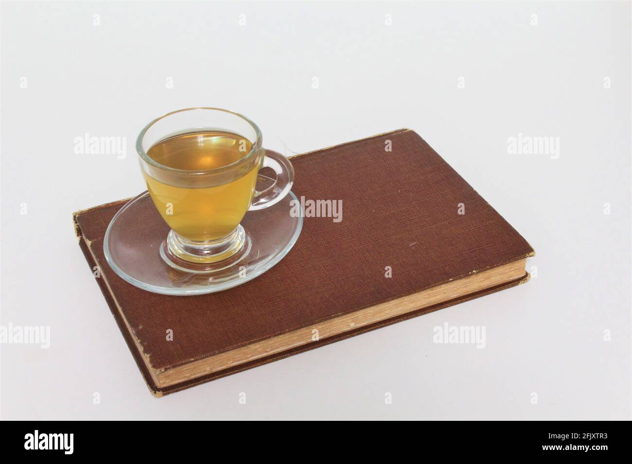 Tasse Kräutertees in einer Glas-Teetasse, serviert über einer Untertasse auf einem alten Vintage-Buch. Auf einem schlichten weißen Hintergrund Stockfoto