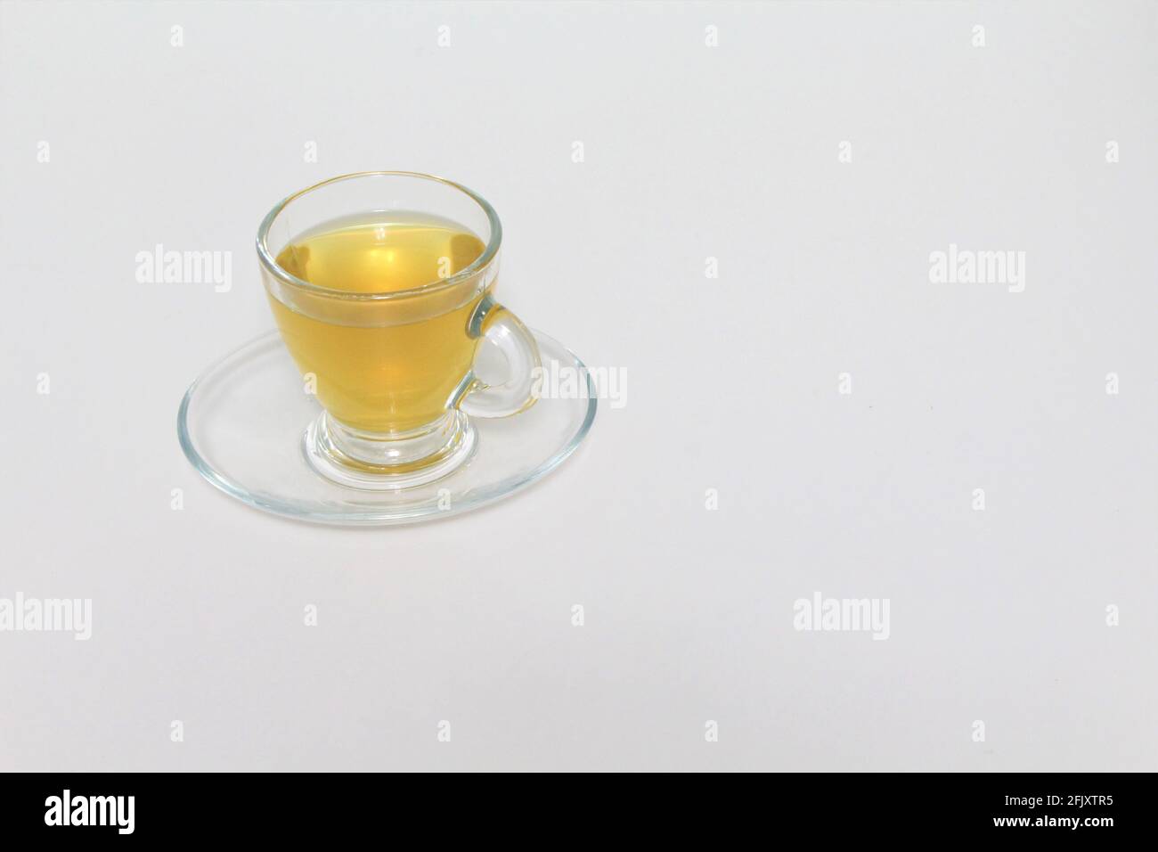 Durchsichtige Teetasse mit Untertasse, gefüllt mit grünem Tee auf weißem, isoliertem Hintergrund. Speicherplatz kopieren Stockfoto