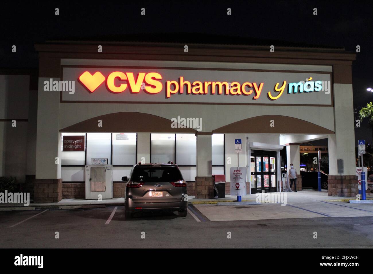 Nachtaufnahme des Eingangs eines CVS, das auch Spanisch in seine Schilder integriert hat. CVS y Mas. Ort, an dem COVID-19-Impfstoffe verabreicht werden Stockfoto