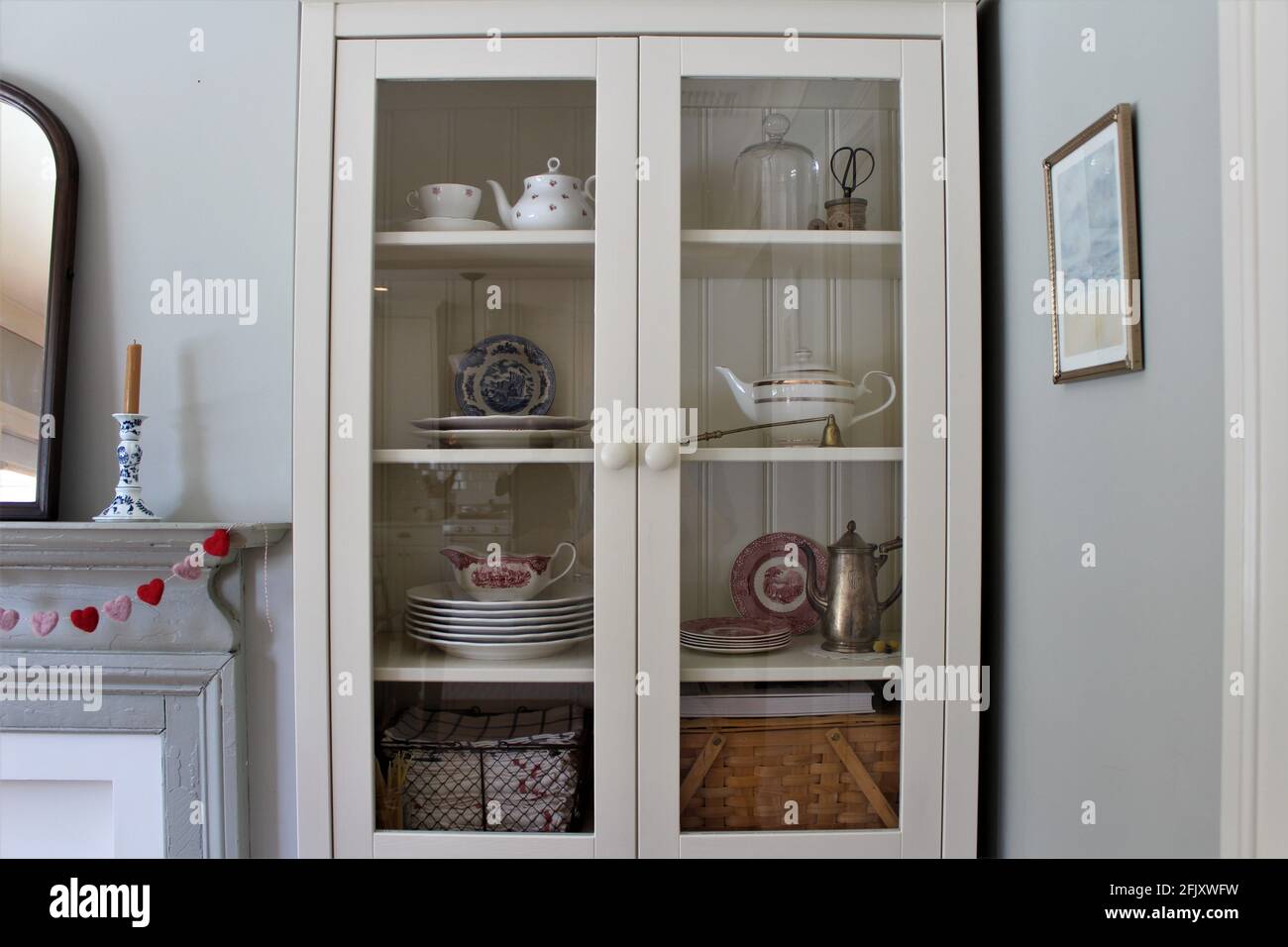 Weißer Holzschrank mit klarem Glas zur Aufbewahrung von Teekannen, Tellern, Teetassen und anderen Küchenzubehör. Stockfoto