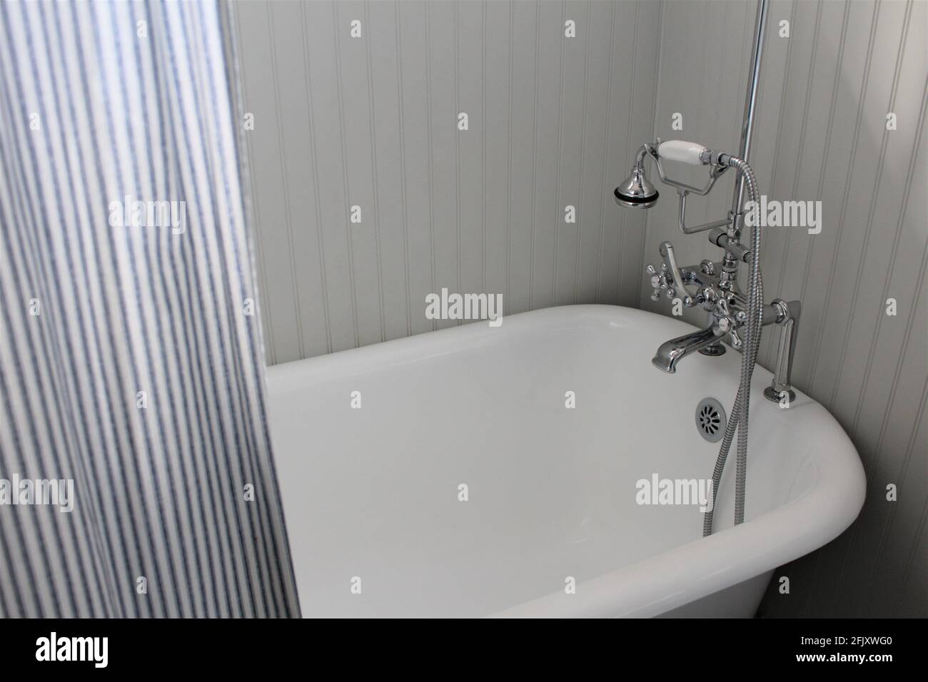 In einer weißen Badewanne mit Clawfoot und gestreiftem Vorhang kann das Wasser aus der Badewanne fliessen. Stockfoto
