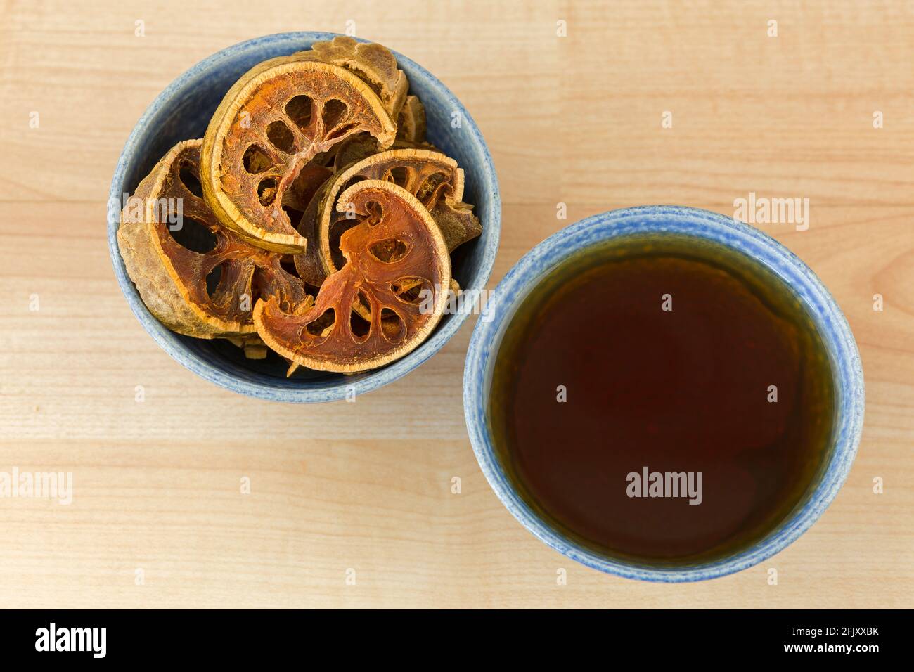 Sonnengetrocknete Bael-Früchte in Schale neben einer Tasse heißen Bael-Kräutertee, auch Steinapfel genannt, Draufsicht auf Holzhintergrund (Aegle Marmelos) Stockfoto