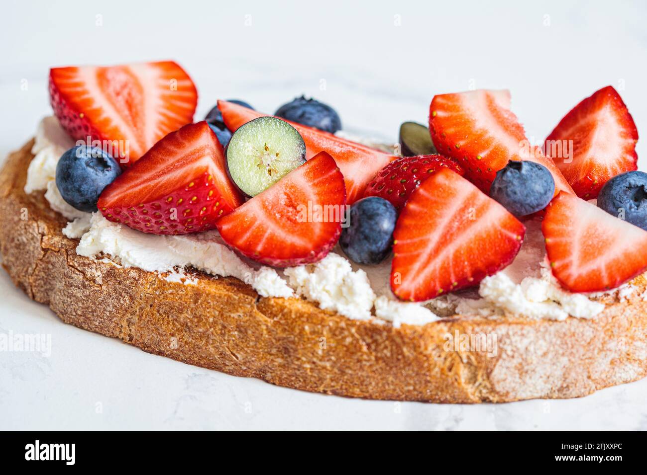 Toast mit Frischkäse, Erdbeeren, Heidelbeeren und Ahornsirup. Sommerliches Food-Konzept. Stockfoto