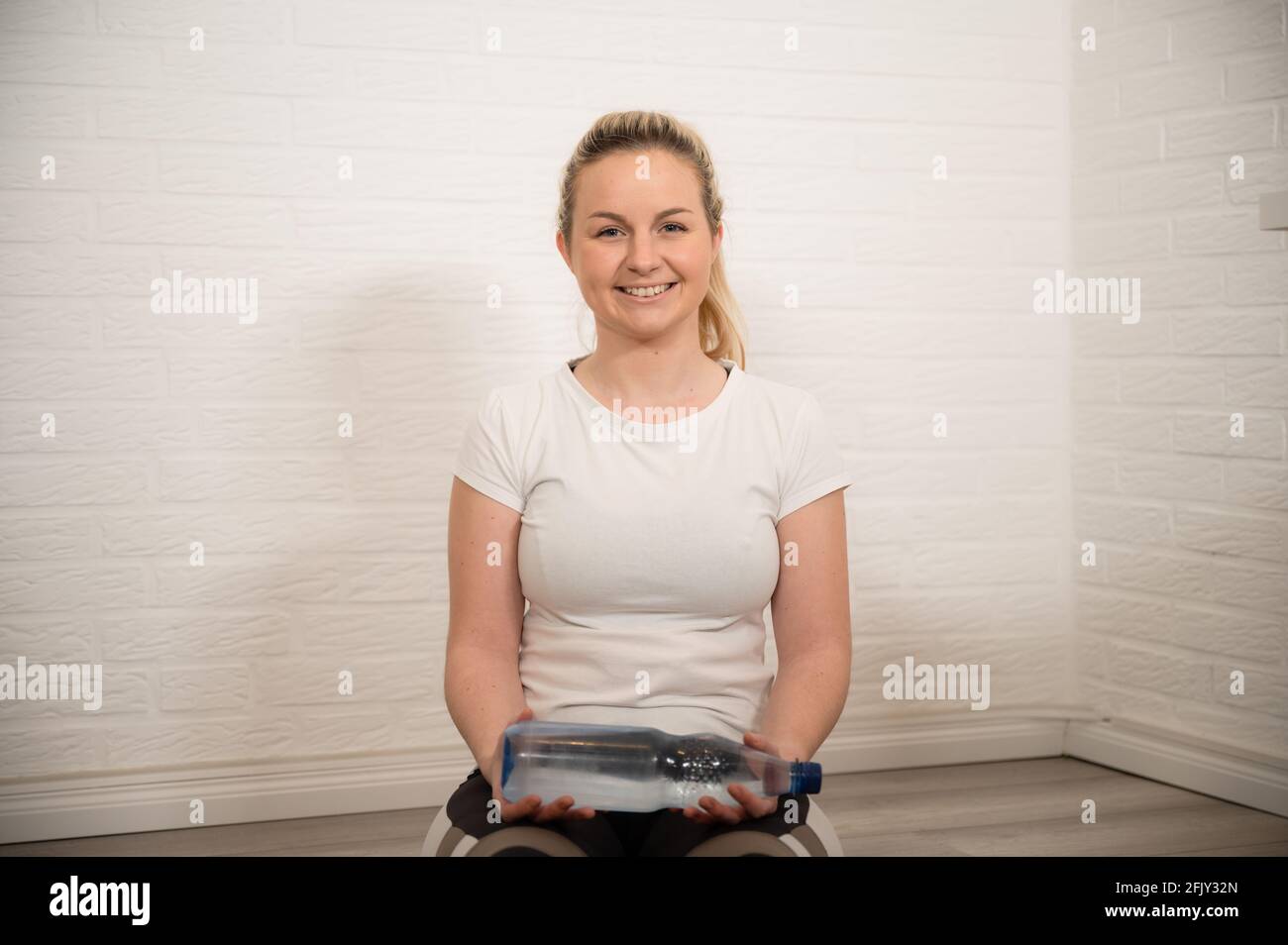 Glückliche blonde Frau macht Fitness-Übung mit Wasserflaschen - Basic Sport Workout als Training zu Hause Stockfoto