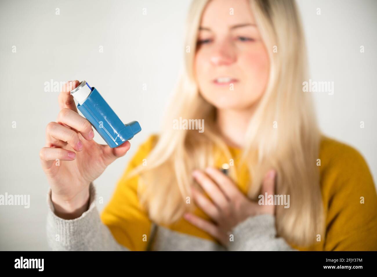 Junge blonde Frau, die einen Asthmaspray-Inhalator in sich hält Hand Stockfoto