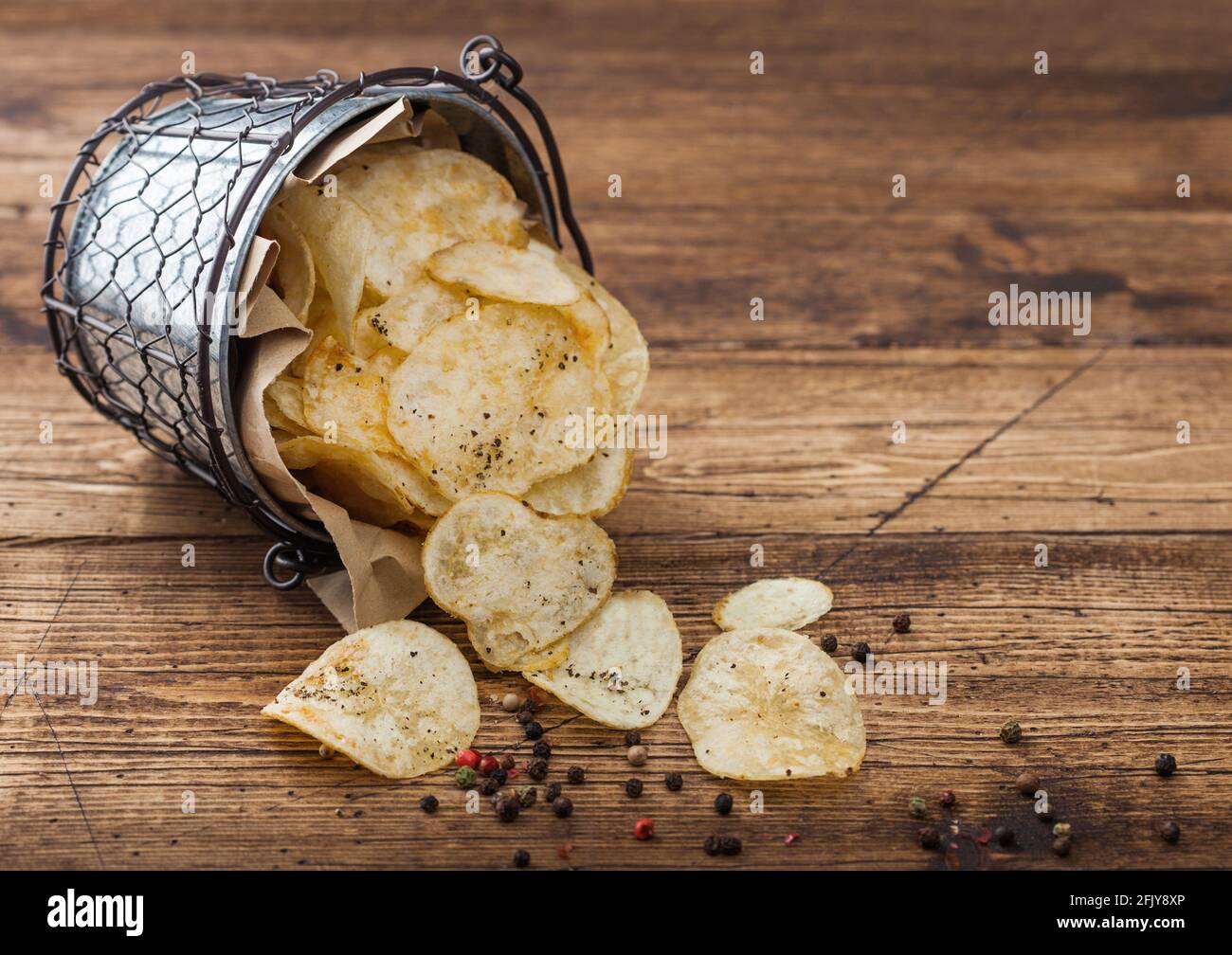Kartoffelchips Chips mit schwarzem Pfeffer in Stahl-Snack-Eimer auf Holztisch Hintergrund. Bester Snack für Bier und Limonade. Stockfoto