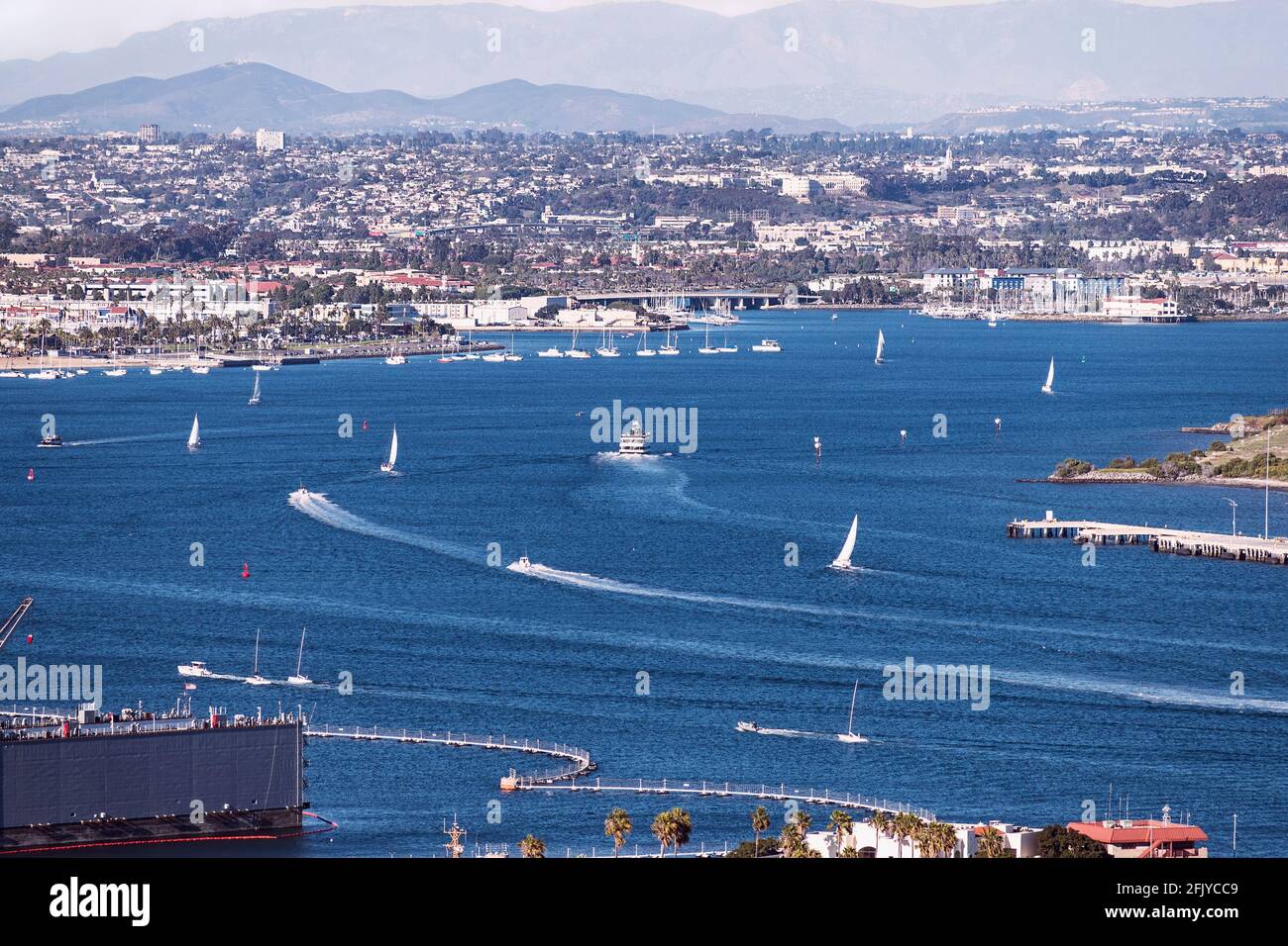 Segelboote und Hafenkreuzfahrtschiffe lassen ihr Wachen auf dem west End der San Diego Bay mit der Stadt Und verschwommene Berge im Hintergrund Stockfoto