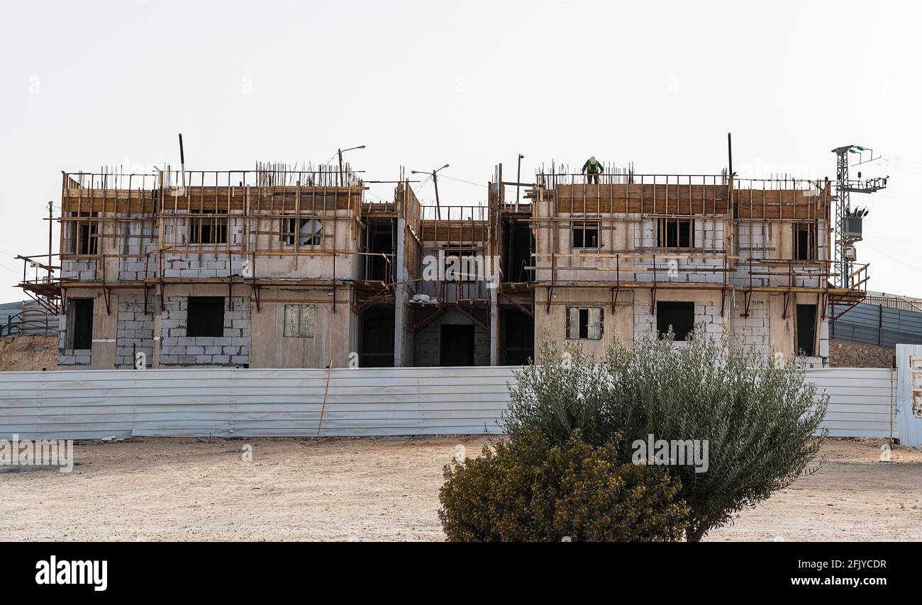 Ein Inspektor auf einem Betonblock darunter Bau in Mitzpe Ramon in Israel hinter einer Metallbarriere Zaun mit Sträuchern Stockfoto