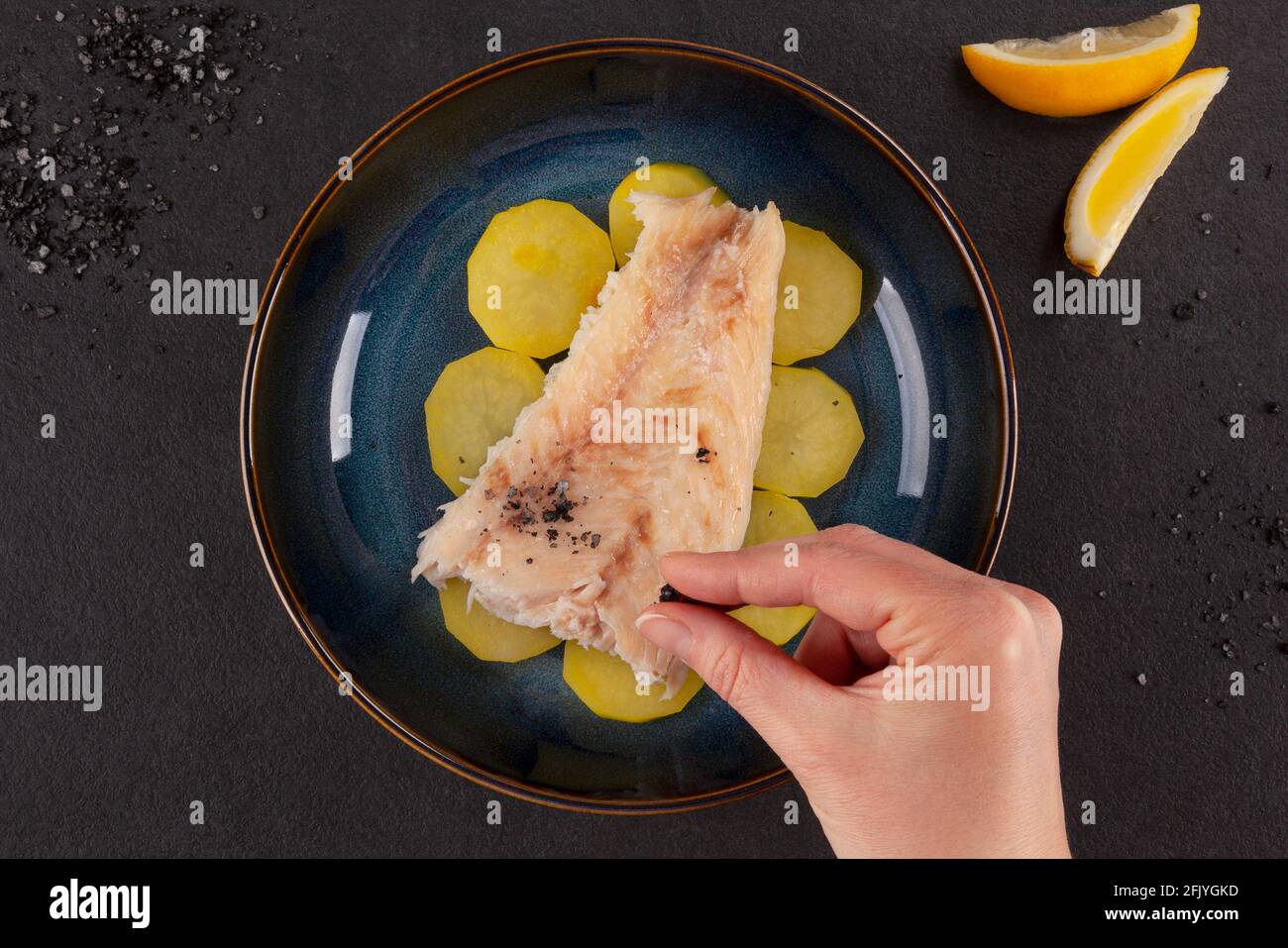 Gegrilltes Fischfilet mit Kartoffeln und Lavasalz auf dunklem Hintergrund. Stockfoto