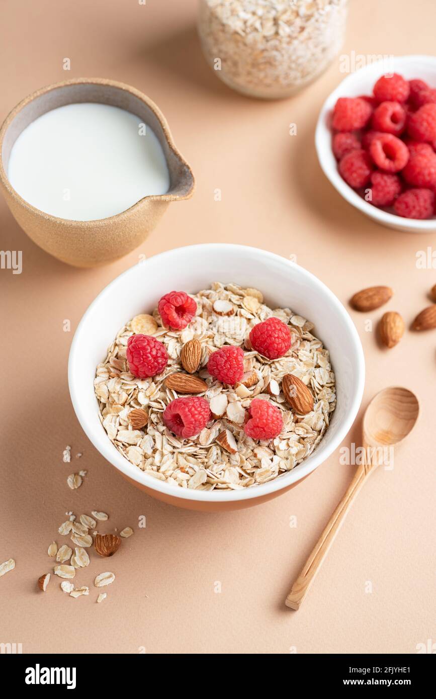 Hafermüsli mit Mandeln und Himbeeren in einer Schüssel. Gesundes Frühstück, sauberes Essen, Diät-Konzept. Beigefarbener Hintergrund Stockfoto