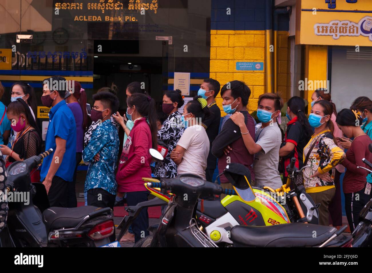 Keine soziale Distanzierung, kein Chaos als kambodschanische Arbeiter in der Bekleidungsfabrik, die Schutzmasken / -Abdeckungen tragen, sich bei einer Bank anstellen, um ihre Löhne zu sammeln, schließt Phnom Penh am ersten Tag vor dem kambodschanischen Neujahr während der Coronavirus-Pandemie alle Straßen in und aus der Stadt. Steung Meanchey, Phnom Penh, Kambodscha. April 2020. © Kraig Lieb Stockfoto
