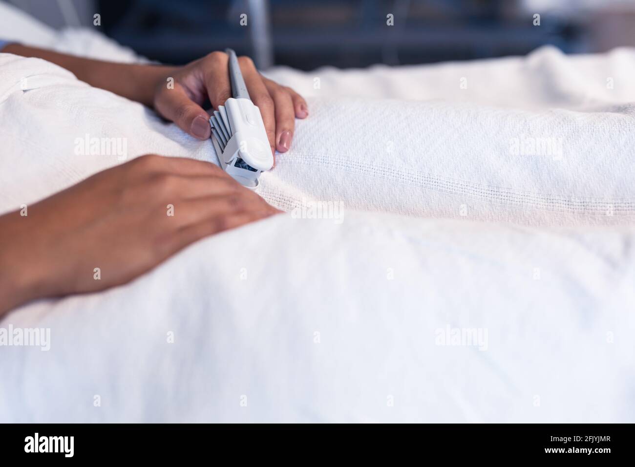 Mittelteil einer weiblichen Patientin mit gemischter Rasse, die im Krankenhausbett liegt Tragen des Pulsoximeters mit der Fingerspitze Stockfoto