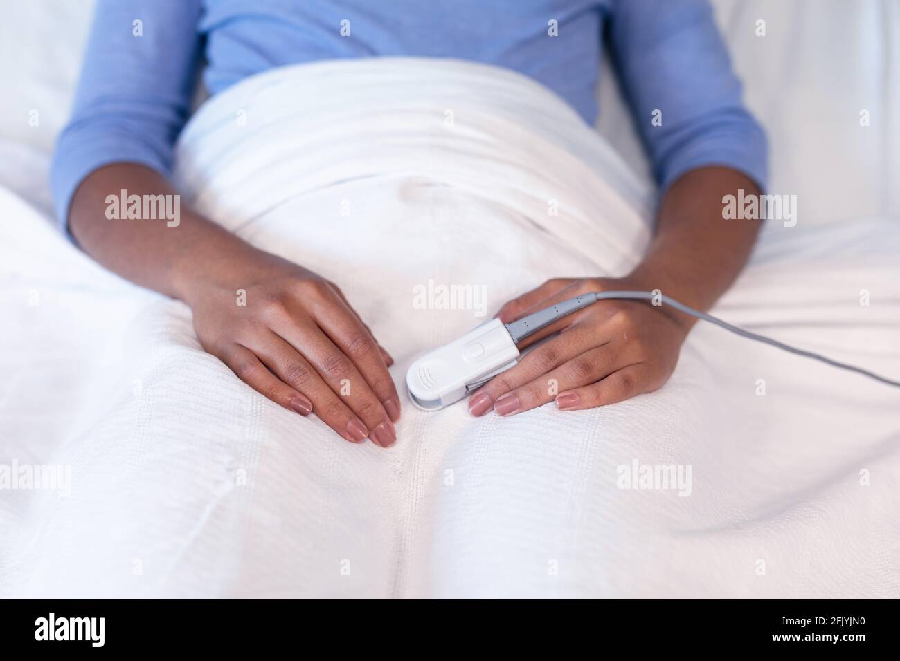 Mittelteil einer weiblichen Patientin mit gemischter Rasse, die im Krankenhausbett liegt Tragen des Pulsoximeters mit der Fingerspitze Stockfoto