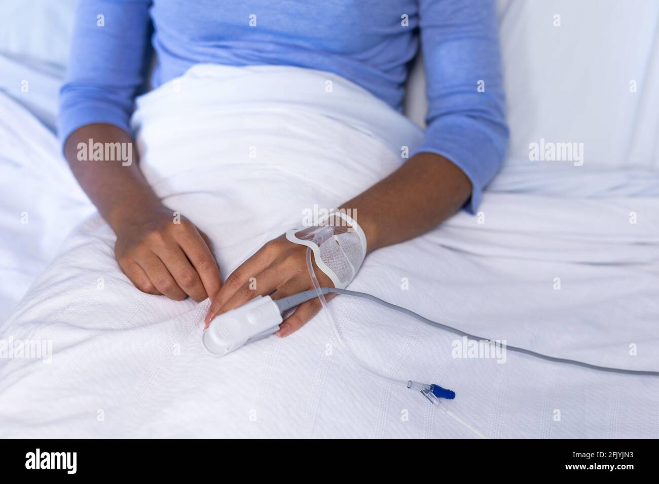 Mittelteil einer weiblichen Patientin mit gemischter Rasse im Krankenhausbett Pulsoximeter mit Fingerspitze und infusionsschlauch Stockfoto