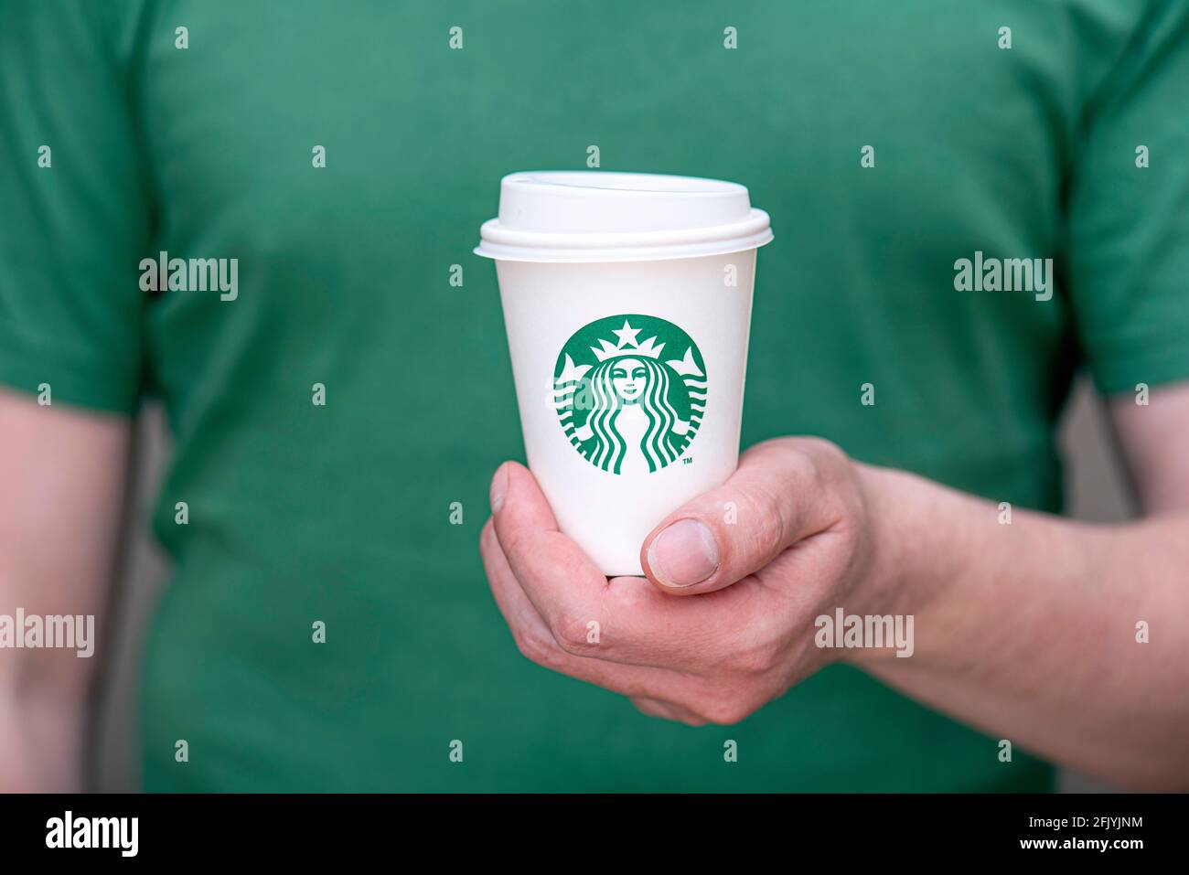BERLIN - APR 25: а Mann in grünem T-Shirt mit weißem Papierbecher mit Starbucks-Logo im Starbucks-Restaurant in Berlin, April 25. 202 in deutscher Sprache Stockfoto