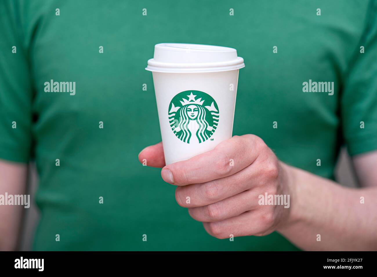 BERLIN - APR 25: а Mann in grünem T-Shirt mit weißem Papierbecher mit Starbucks-Logo im Starbucks-Restaurant in Berlin, April 25. 202 in deutscher Sprache Stockfoto