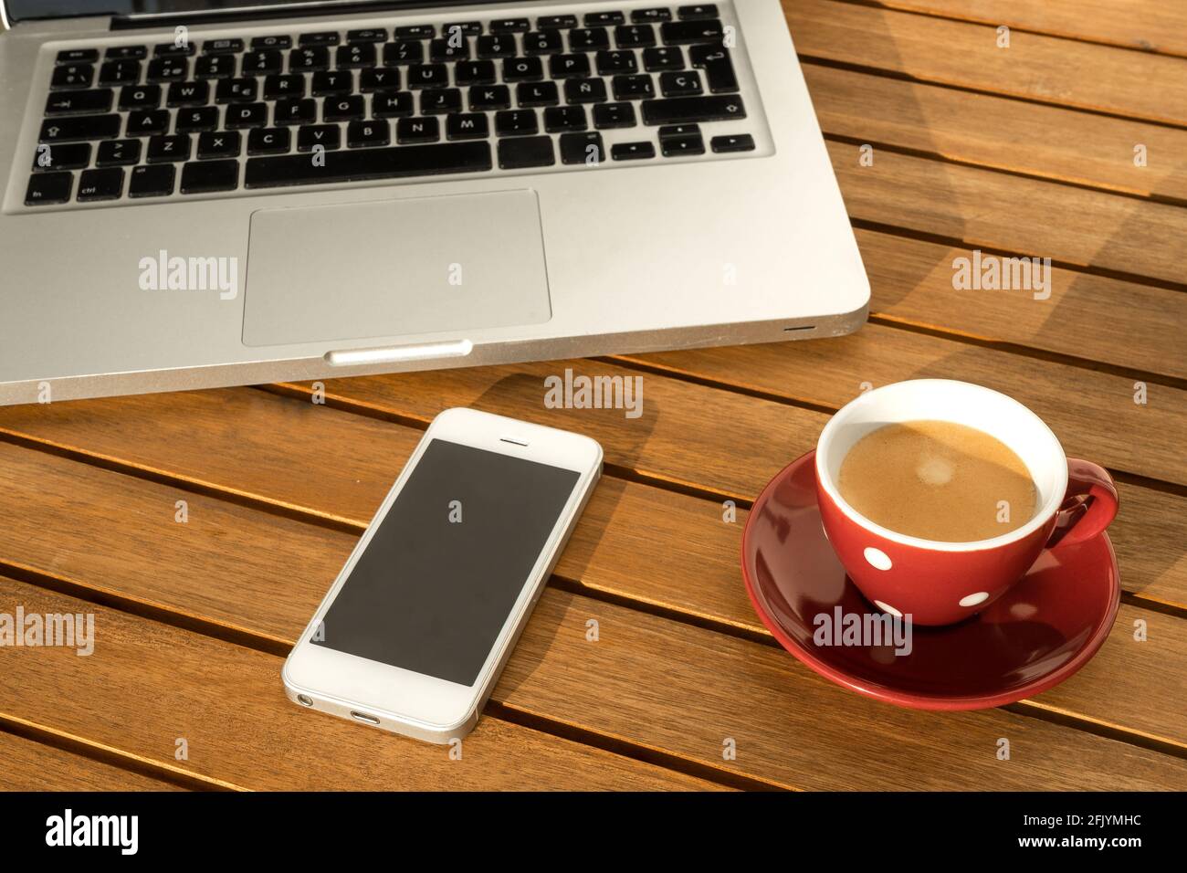 Laptop-Computer neben Tasse mit Kaffee und Handy, auf Holztisch auf der Terrasse. Stockfoto