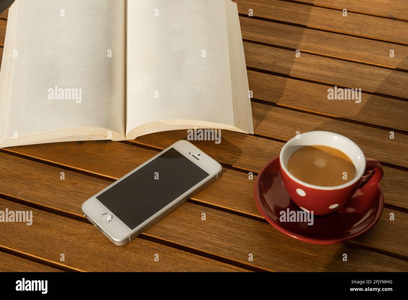 Leeres Buch, Mobiltelefon und Kaffeetasse, auf Holztisch. Stockfoto