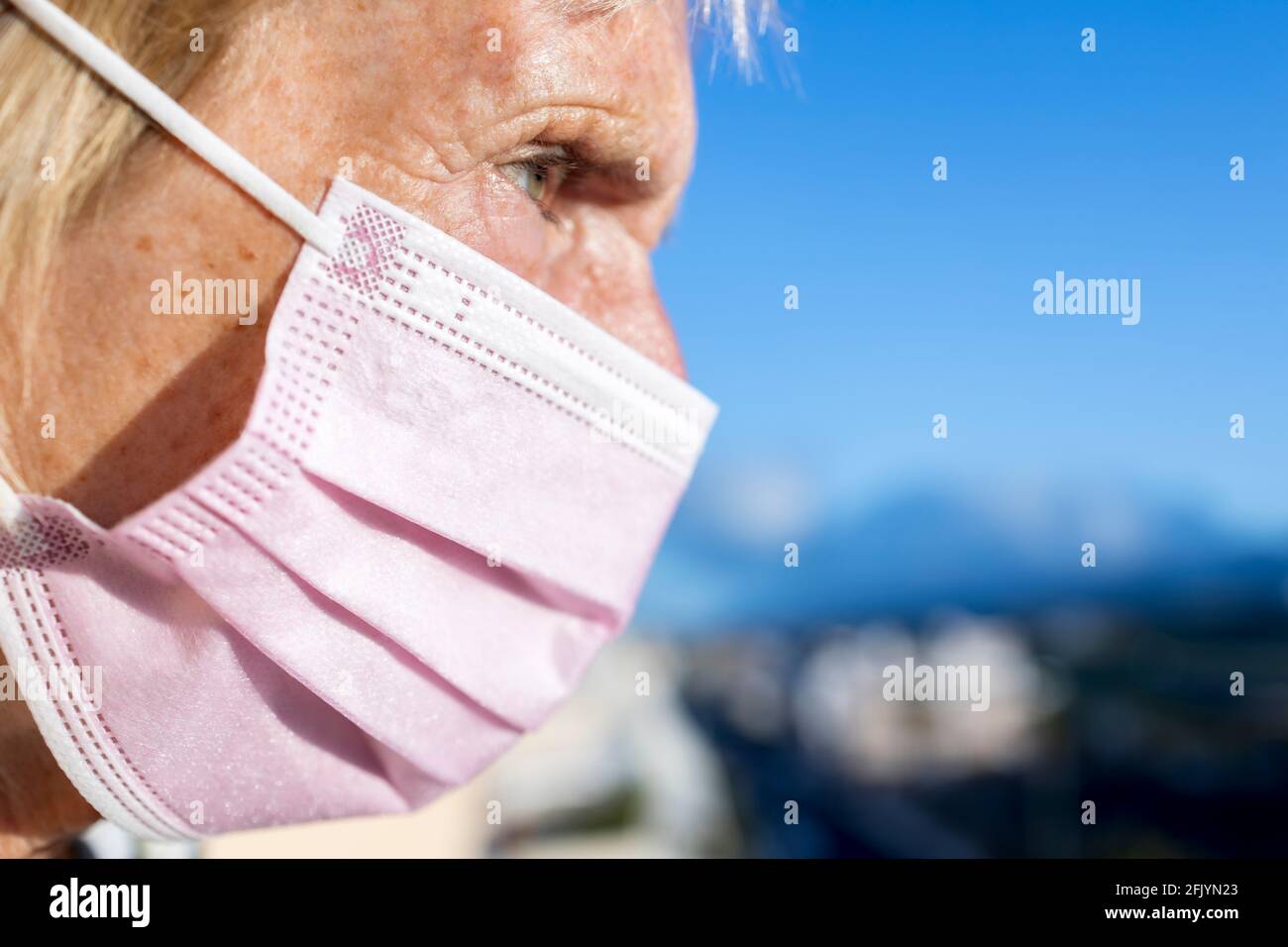Ältere Frau, die während der Coronavirus-Pandemie Covid 19 eine rosa OP-Maske über Mund und Nase trug, mit blauem Himmel Hintergrund Stockfoto