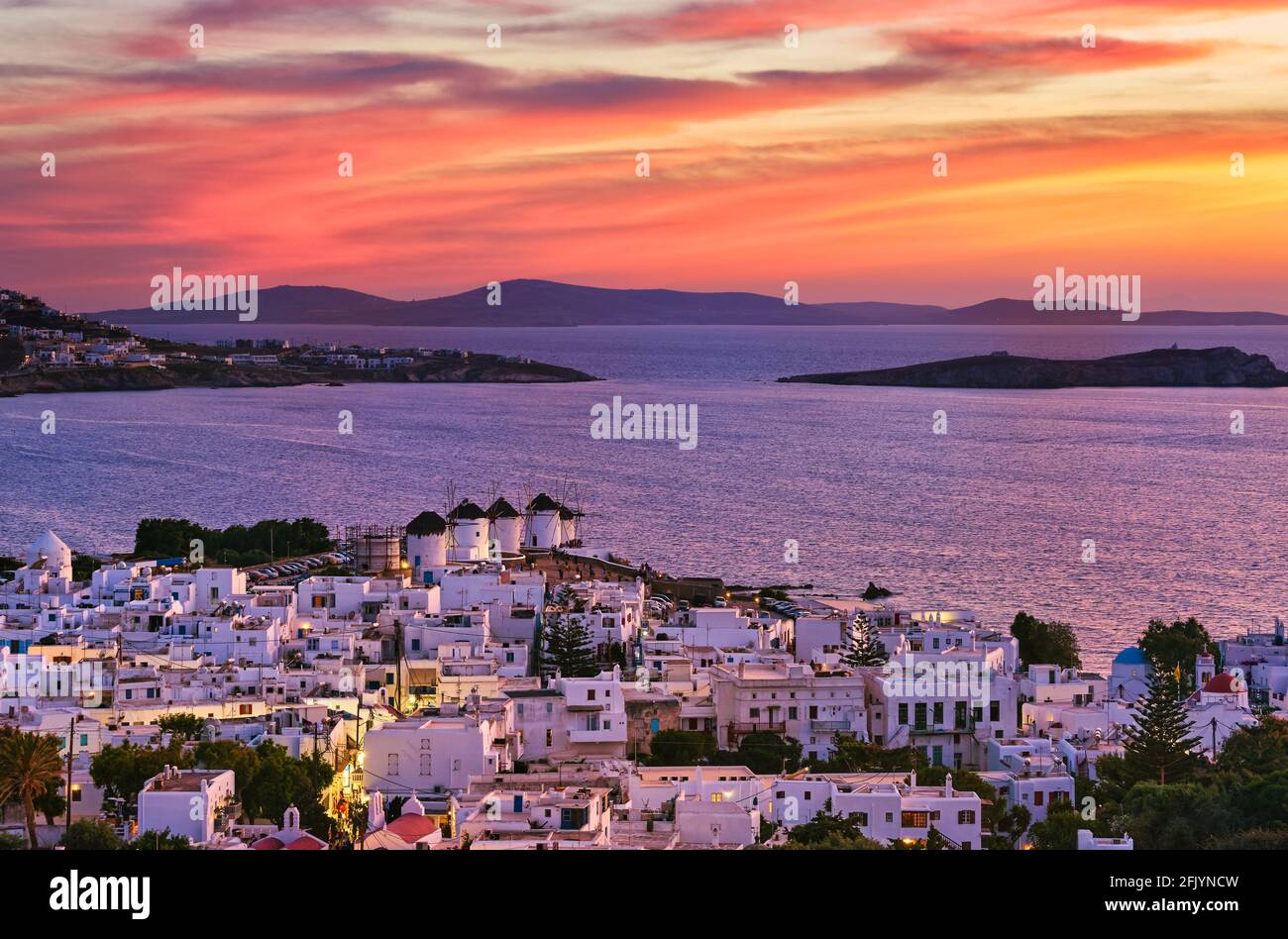 Wunderschöne Sonnenuntergangsansicht der berühmten traditionellen weißen Windmühlen auf dem Hügel, Mykonos, Griechenland. Weiß getünchtes Haus, farbenprächtiger Sonnenuntergang, Sommer, Stadtlicht an Stockfoto